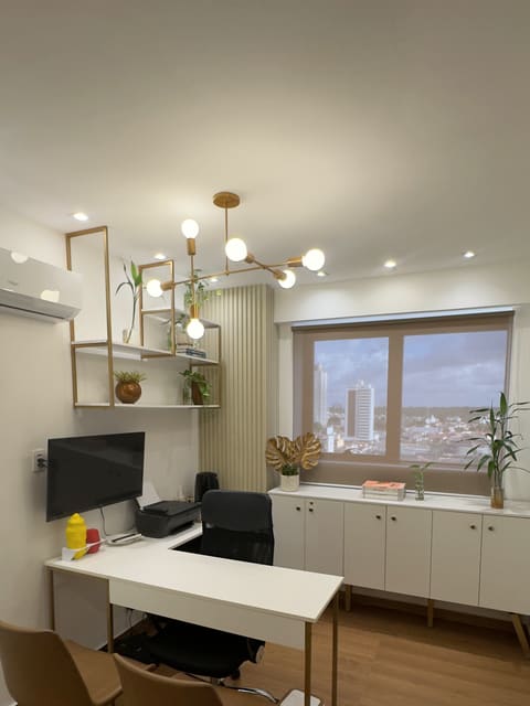 Vista ampla da sala, com o lustre, as prateleiras douradas e a janela ao fundo
