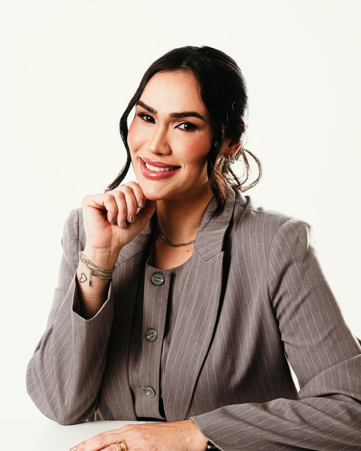 Camila Machado, nutricionista, sentada à mesa com a mão no queixo, sorrindo para a câmera